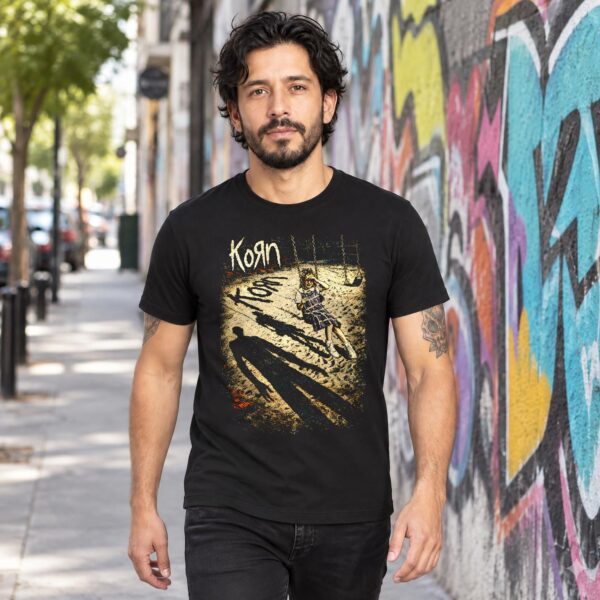 Hombre caminando en la calle con playera negra de Korn del primer álbum junto a un muro con grafiti