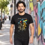 Hombre con playera negra Pink Floyd de astronautas y prisma caminando junto a un muro con grafiti