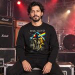 Hombre sentado en escenario con sudadera negra Pink Floyd de astronautas y prisma