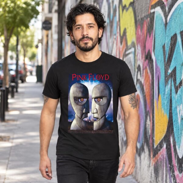 Hombre con playera negra de Pink Floyd cabezas metálicas caminando junto a un muro con grafiti