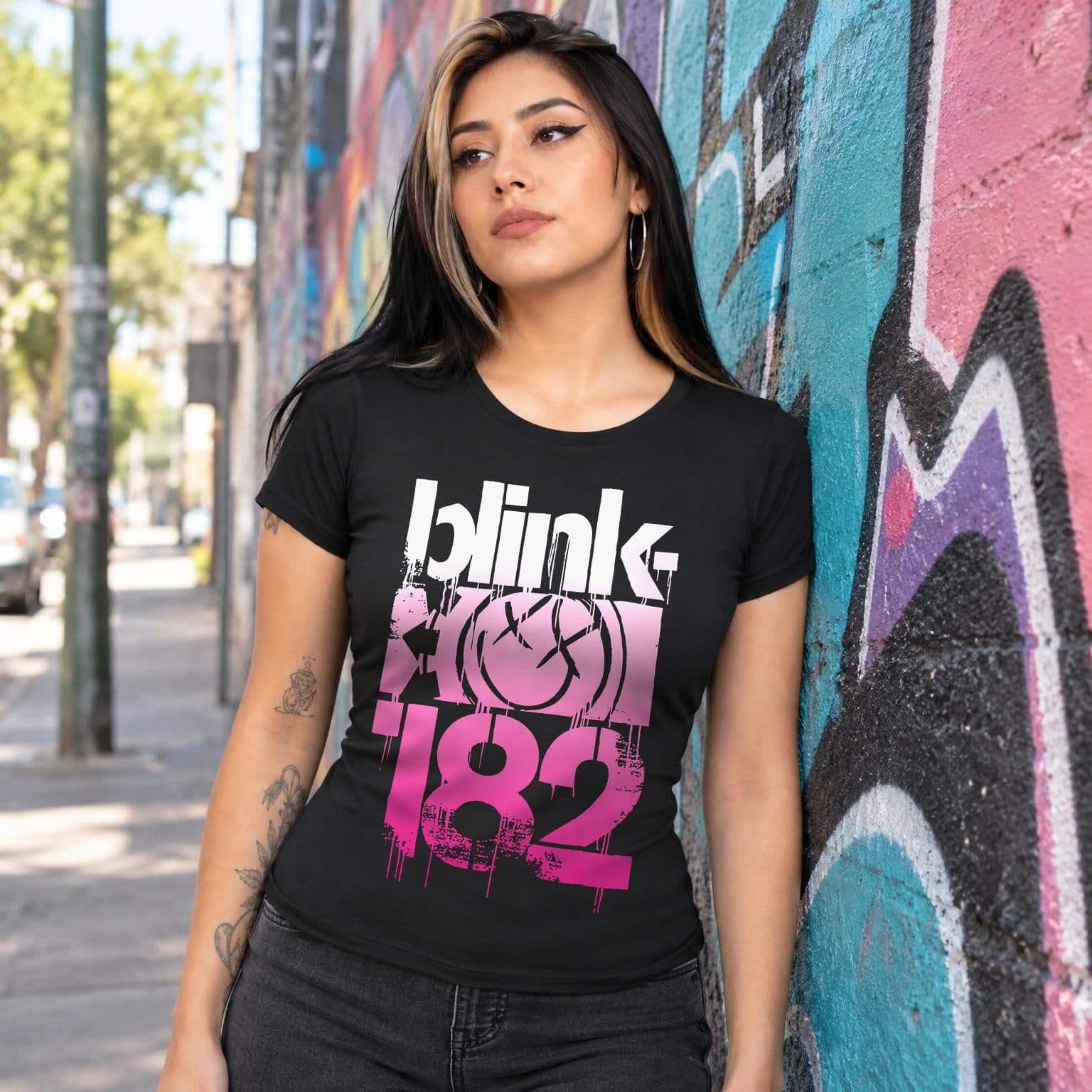 Modelo con playera negra corte dama de Blink 182 en calle con grafiti