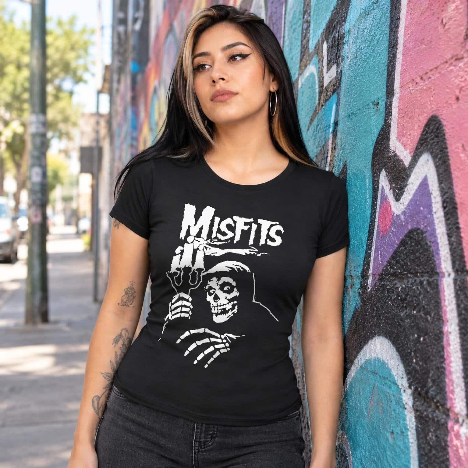 Modelo con playera negra corte dama de Misfits en calle con grafiti